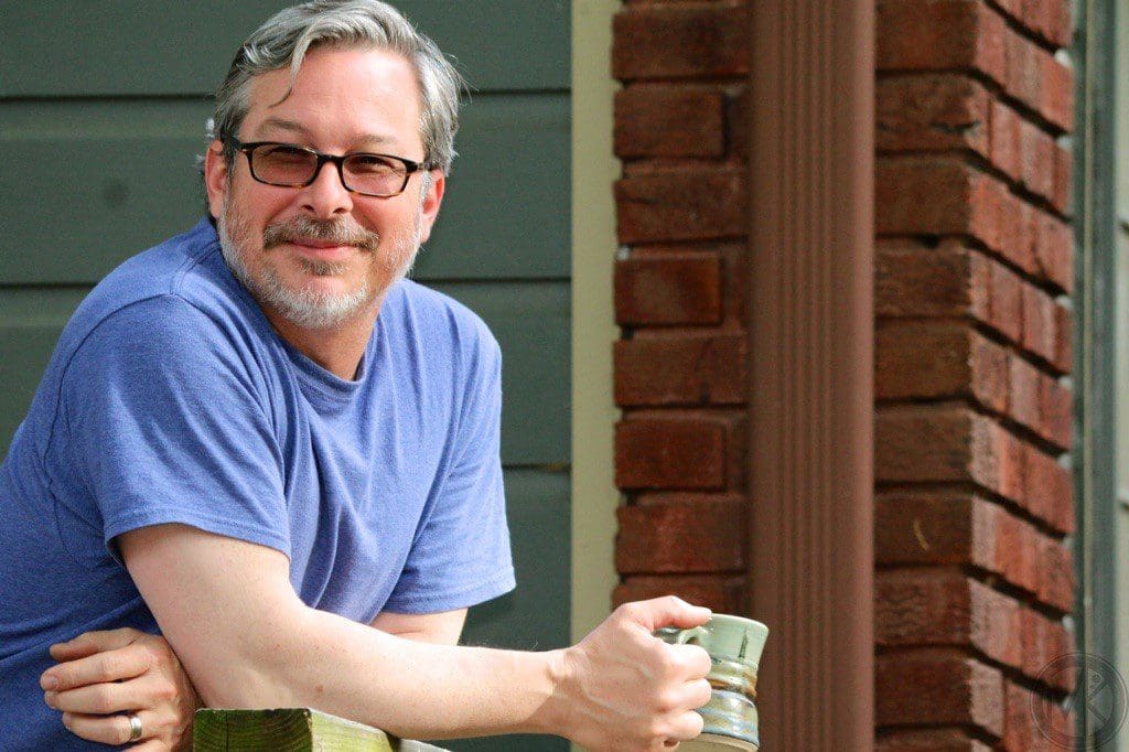 Man in blue shirt with glasses holding a coffee mug and smiling