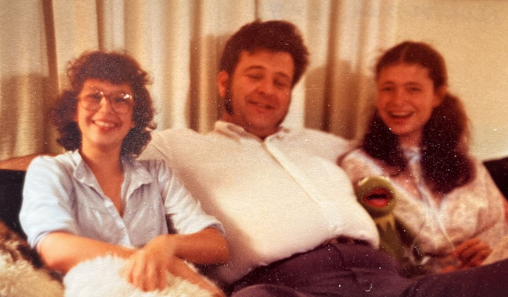 Two daughters sitting with their dad in the middle; the daughter on the left is wearing glasses