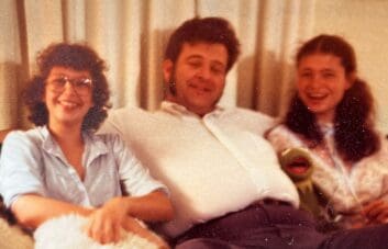 Two daughters sitting with their dad in the middle; the daughter on the left is wearing glasses